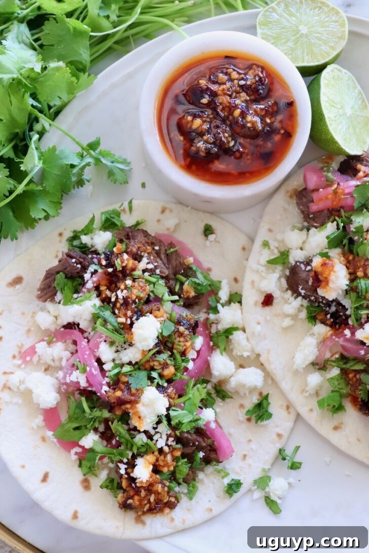 Authentic Mexican Barbacoa Seasoning Recipe 7 shredded beef barbacoa tacos on a plate topped with salsa macha, pickled onions, and cilantro