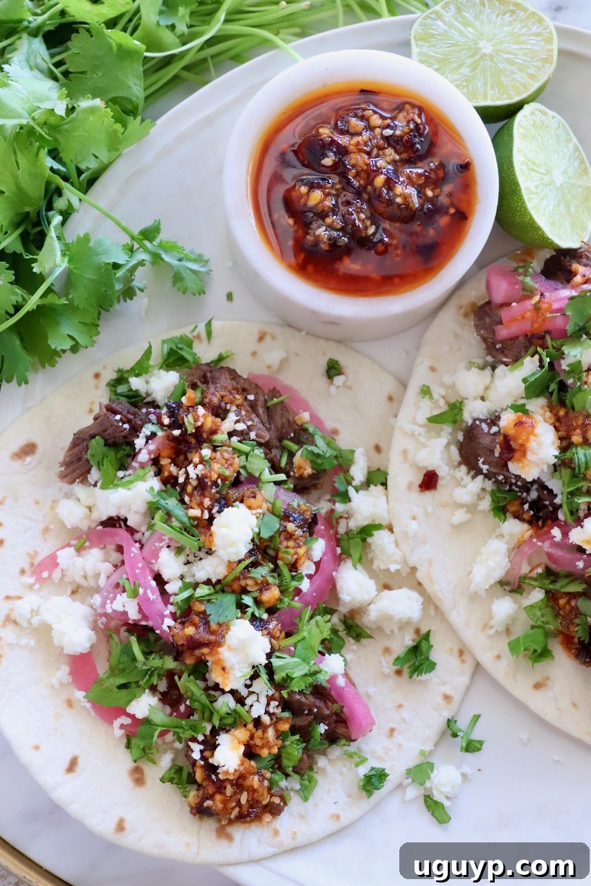 Instant Pot Beef Barbacoa - Tender Shredded Mexican Beef 2 shredded beef barbacoa tacos on a plate topped with salsa macha, pickled onions, and cilantro