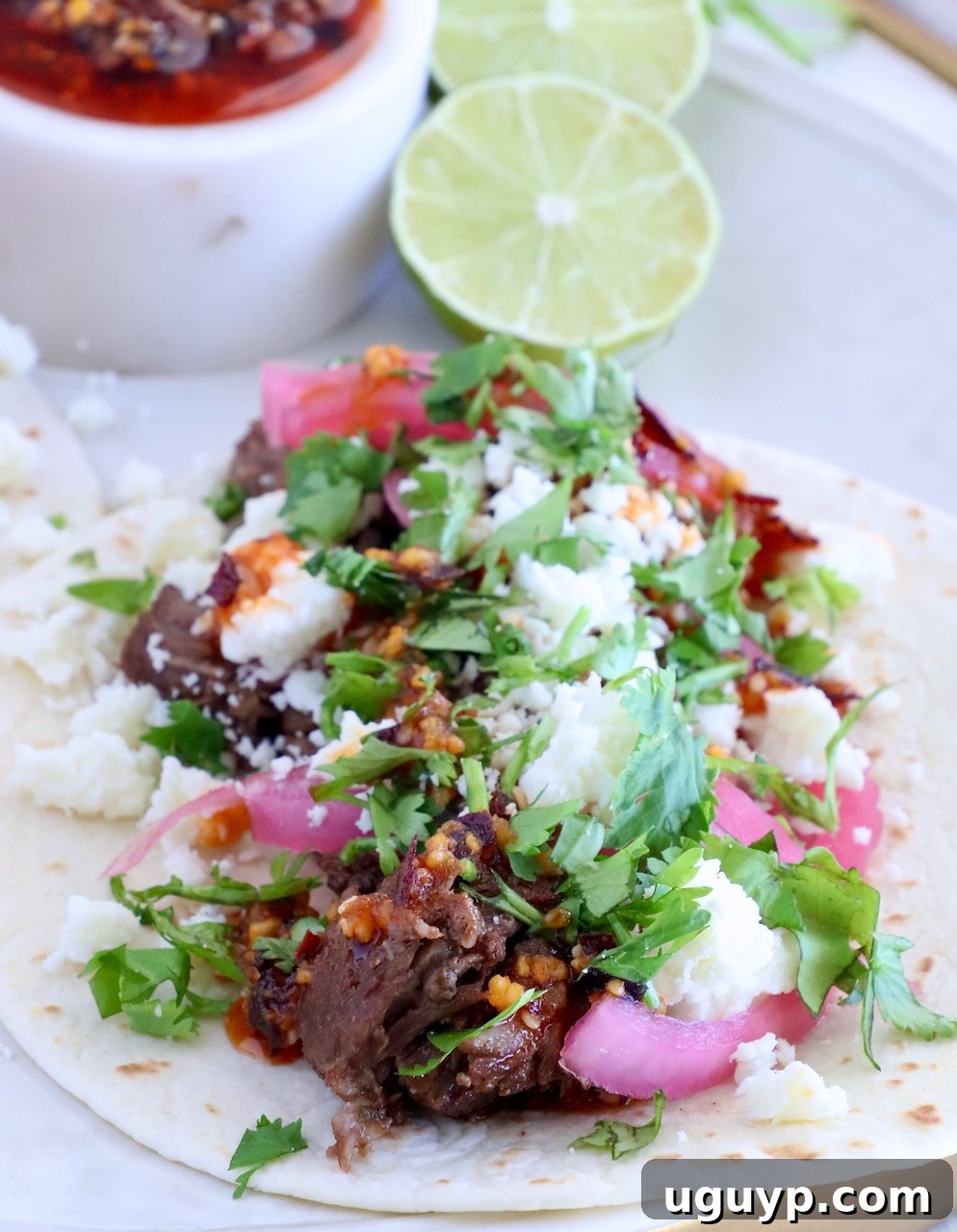 Instant Pot Beef Barbacoa - Tender Shredded Mexican Beef 12 beef barbacoa taco on a plate with salsa macha, limes, cilantro, and pickled onions