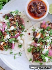 Instant Pot Beef Barbacoa - Tender Shredded Mexican Beef 13 two tacos on a plate topped with beef barbacoa, crumbled cheese, pickled onions, salsa macha, and cilantro