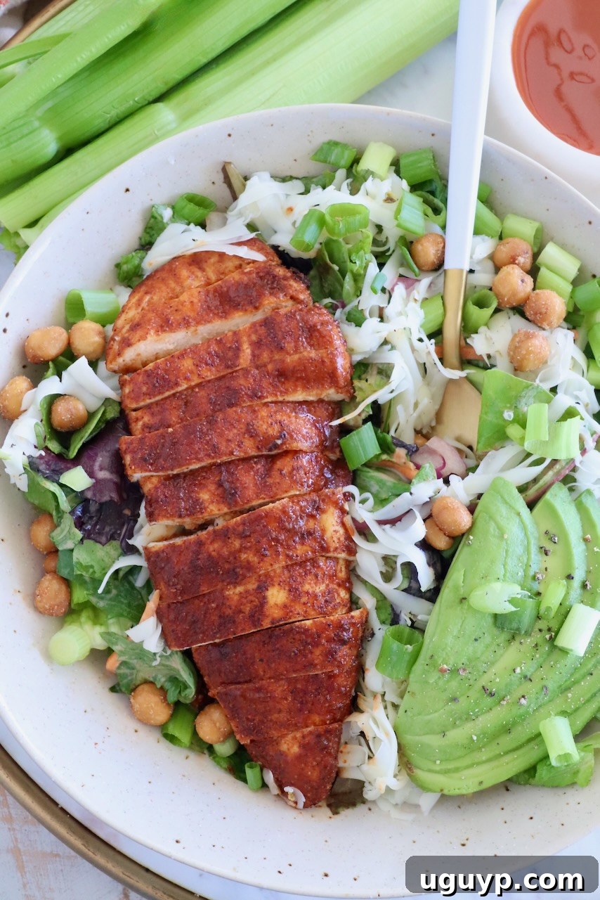 Crispy Buffalo Chicken Salad with Blue Cheese and Ranch 2 sliced buffalo chicken breast on top of a salad in a bowl with sliced avocado and a fork