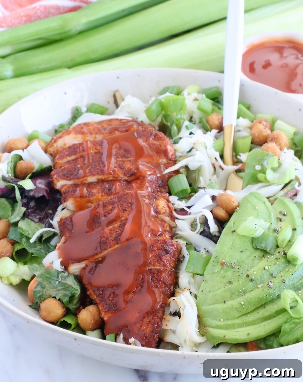 Crispy Buffalo Chicken Salad with Blue Cheese and Ranch 8 sliced chicken topped with buffalo sauce on top of a salad in a bowl with sliced avocado