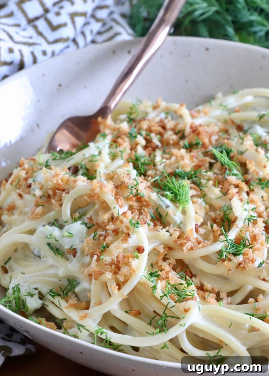 spaghetti tossed in a creamy sauce in a bowl topped with crunchy breadcrumbs and fresh dill