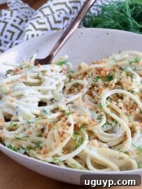 spaghetti in a creamy pickle sauce in a bowl with a fork, topped with toasted breadcrumbs