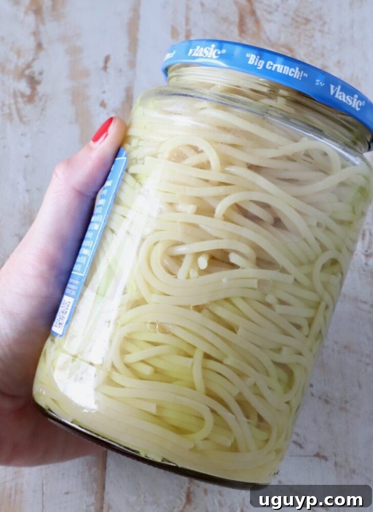 spaghetti noodles in a jar of pickle juice, with a hand holding the jar