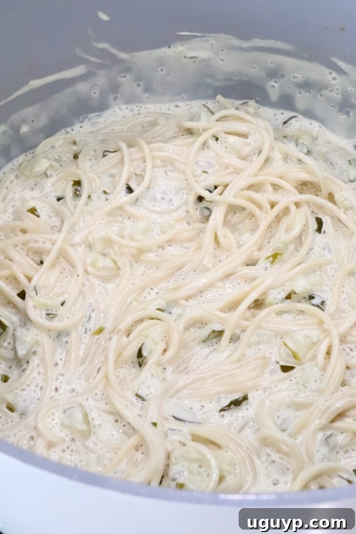 cooking spaghetti noodles in a creamy pickle sauce in a large pot