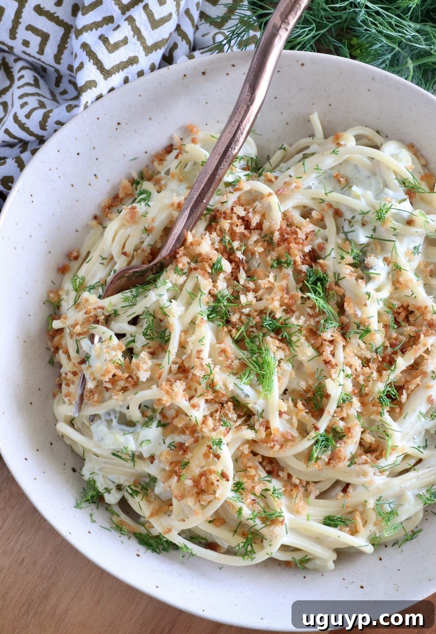 spaghetti tossed in a creamy sauce topped with breadcrumbs and dill in a bowl with a fork
