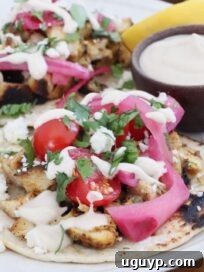 Homemade Chicken Shawarma Tacos Recipe 11 chicken shawarma tacos topped with pickled onions, cilantro, and tomatoes, on a plate with a small bowl of garlic sauce
