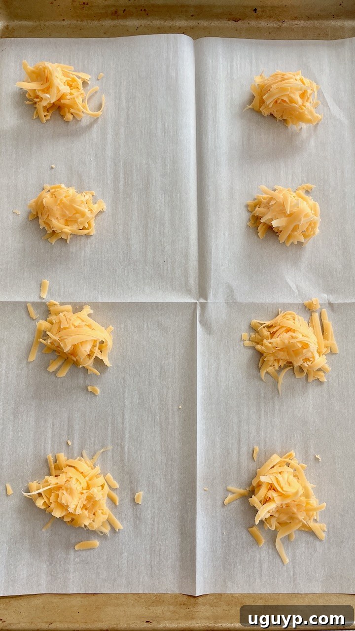small piles of cheddar cheese lined up on a parchment-lined baking sheet