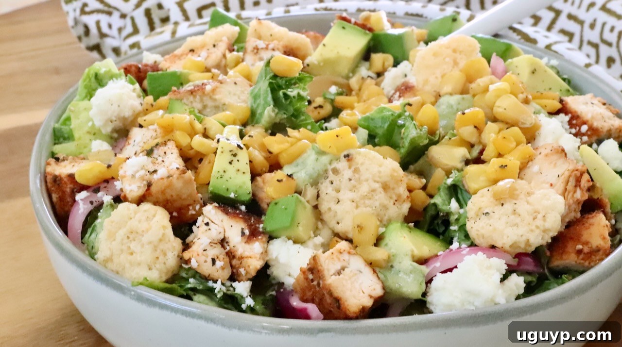 taco salad in a bowl topped with diced chicken, cheese crips, corn and avocado