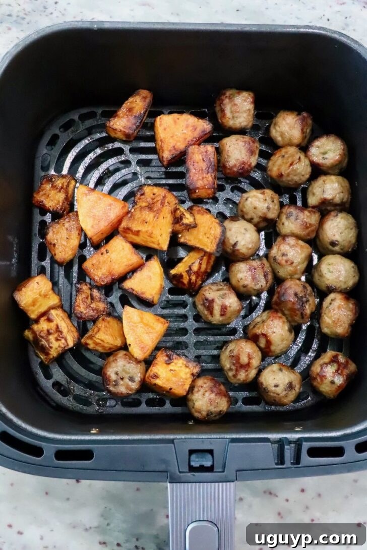 cubed butternut squash and chicken meatballs in an air fryer basket