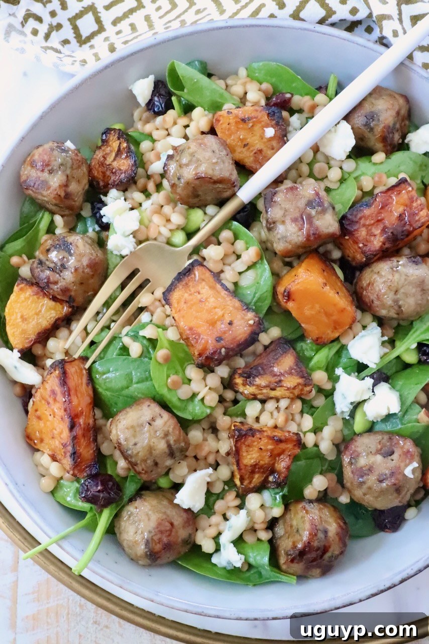 salad in a bowl with a fork, topped with chicken meatballs, butternut squash and couscous
