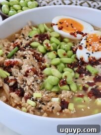 bowl filled with cooked ground chicken, rice, and edamame, covered in broth, chili crisp, and sesame seeds